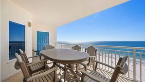 Un balcone con un tavolo rotondo e sedie, una porta blu e vista sulla spiaggia.