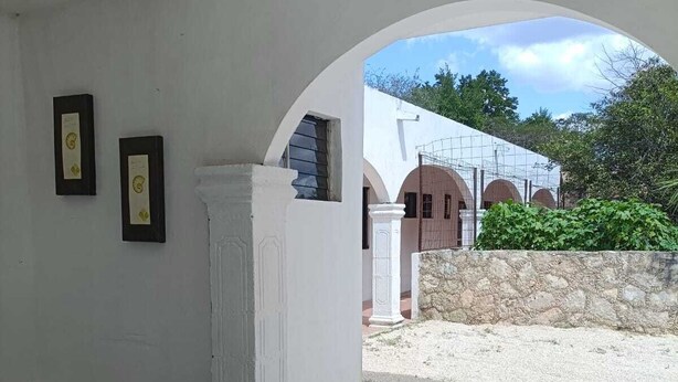 A covered outdoor seating area with a white wall, two framed certificates, and a stone wall in the background. - CASA ALBINO, NICE HOUSE WITH 3 BEDROOMS, VERY COMFORTABLE AND CENTRALLY LOCATED. (Izamal)