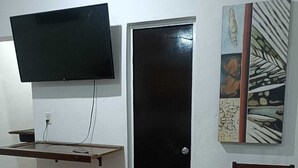 A room with a black door, a mounted TV, a chair, and a wall with a painting. - CASA ALBINO, NICE HOUSE WITH 3 BEDROOMS, VERY COMFORTABLE AND CENTRALLY LOCATED. (Izamal)