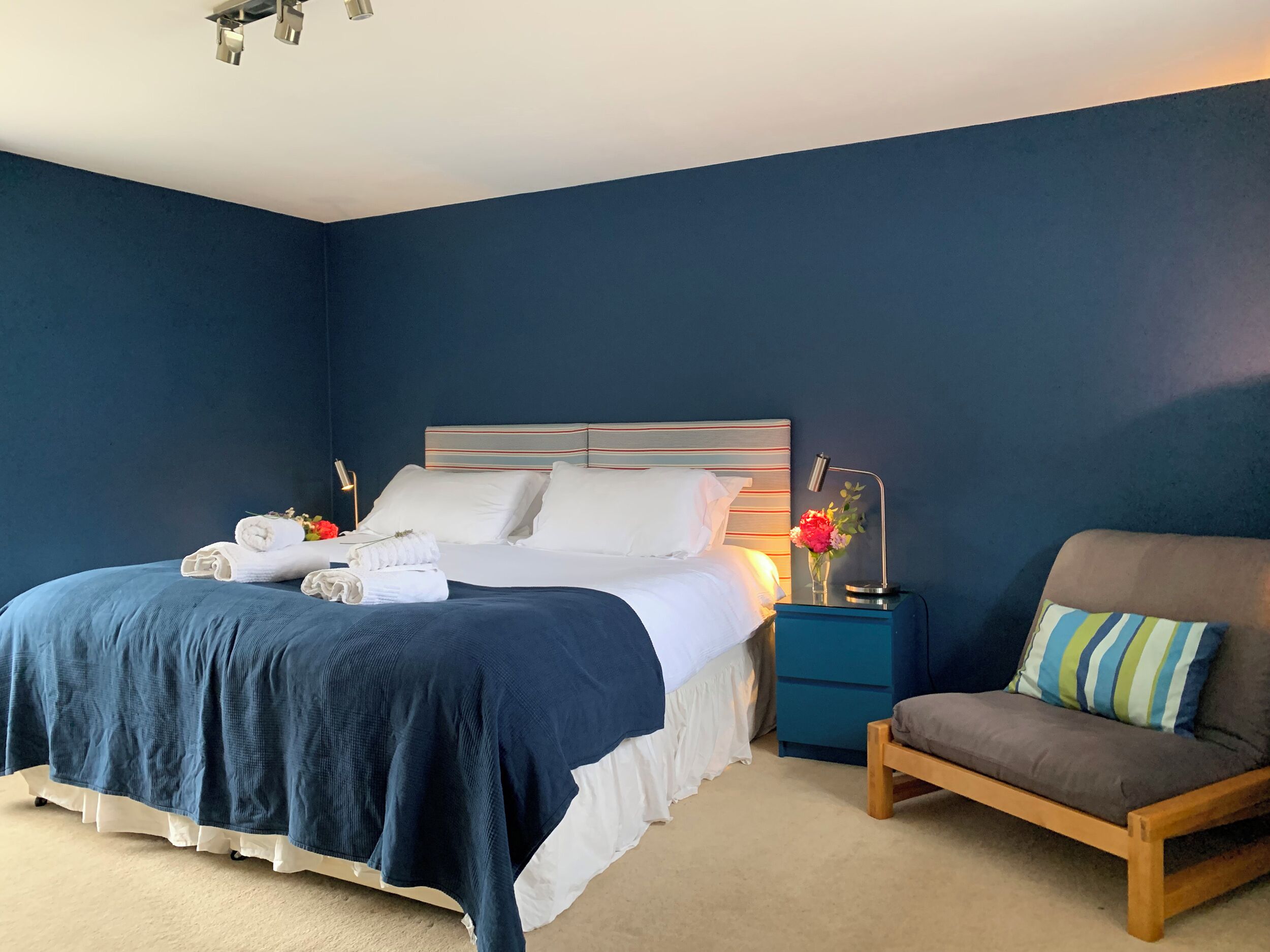 A bedroom with a bed, a nightstand, a chair, and a bedside table.