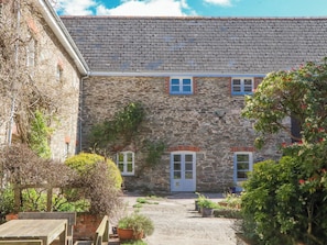 A stone building with a tiled roof, a small garden with potted plants, and a wooden bench. - Chantry (Kingsbridge)