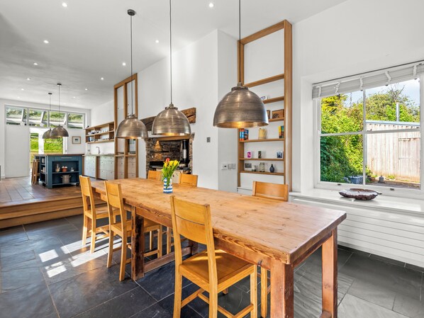 Een ruime keuken met een houten eettafel, hanglampen en uitzicht op de tuin.