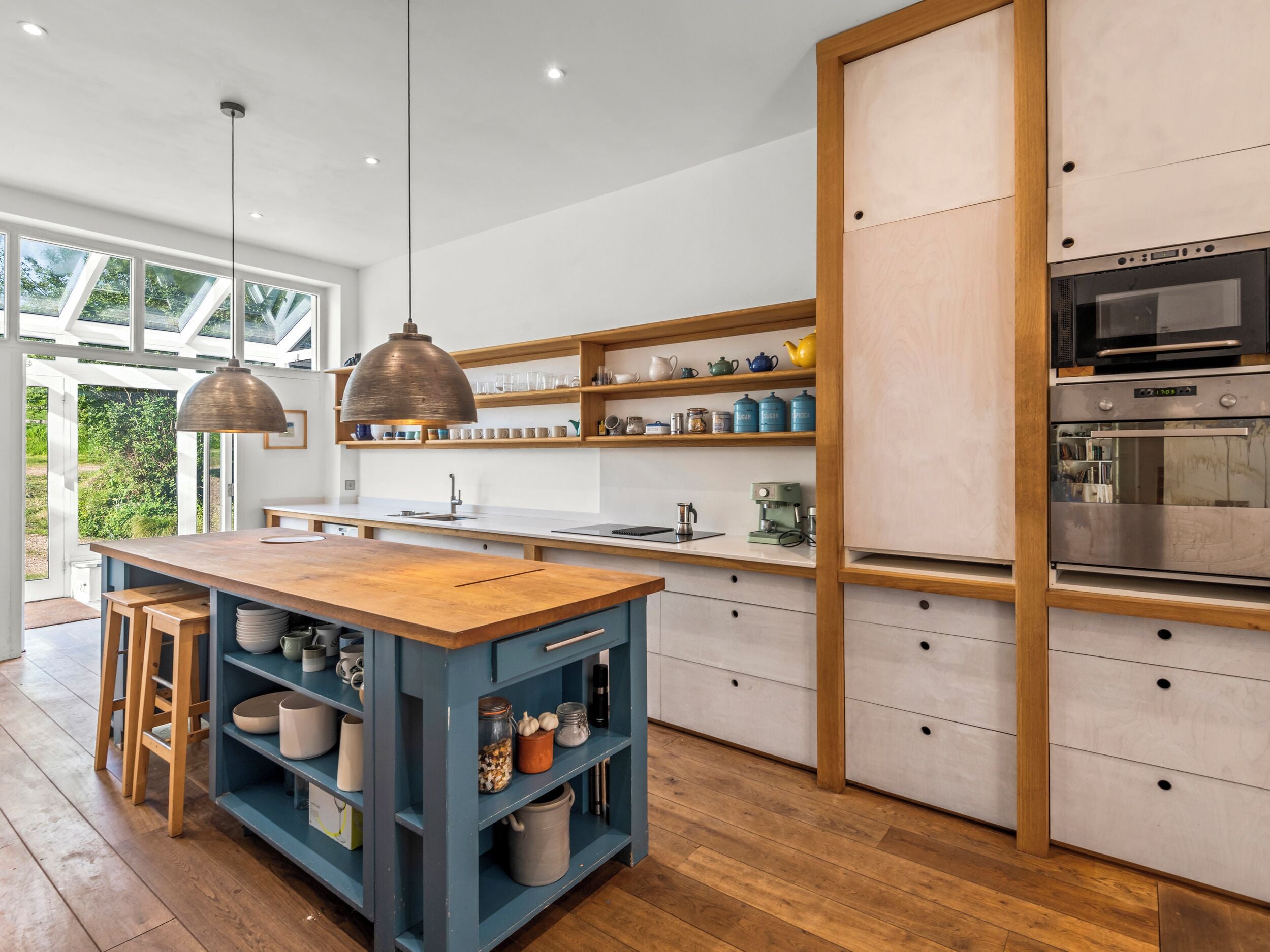 A modern kitchen with wooden countertops, a central island, pendant lighting, and built-in shelving.
