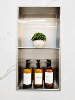 Kylpyhuoneen hyllyllä on kolme pulloa: shampoo, hoitoaine ja suihkugeeli.