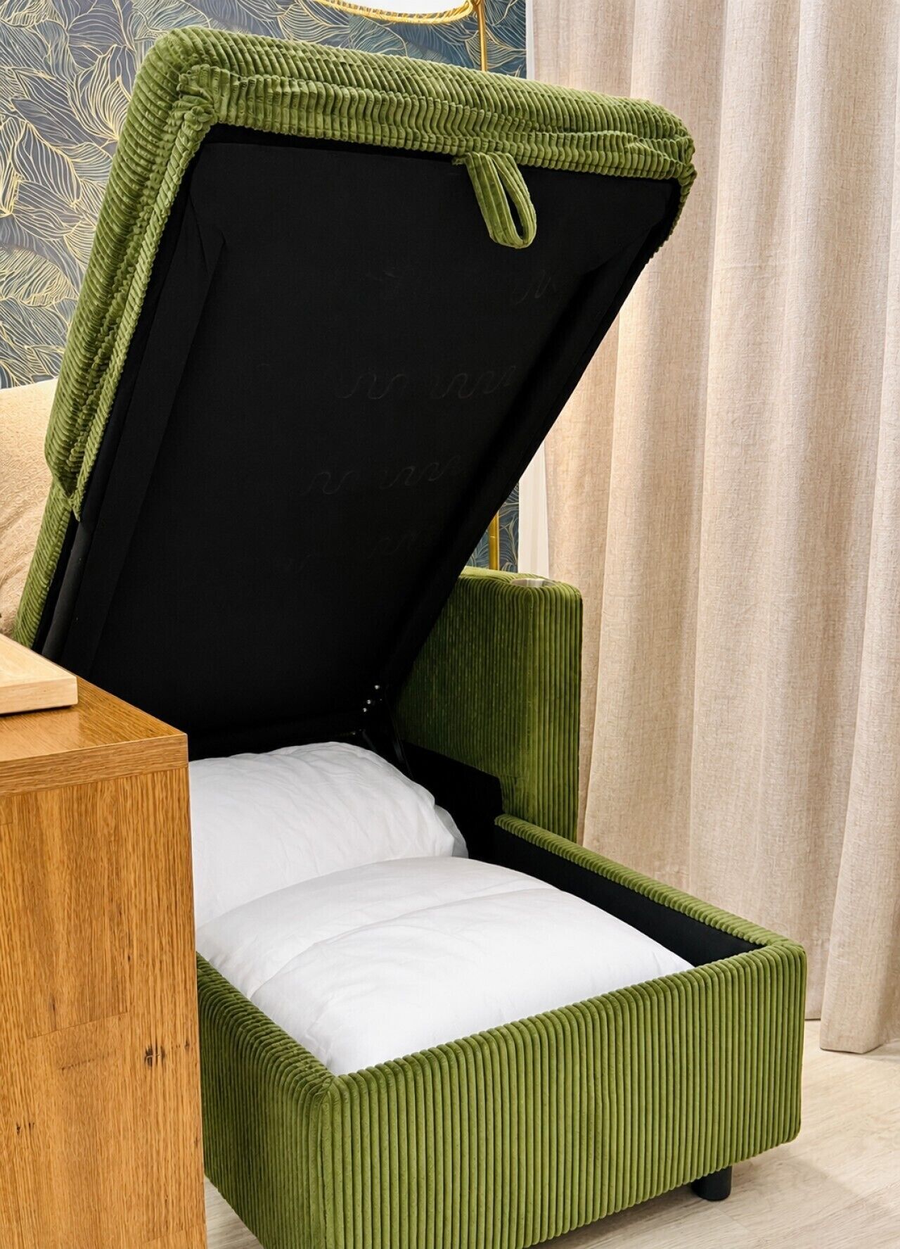 A green upholstered bed with a headboard, a wooden nightstand, and a patterned wall.