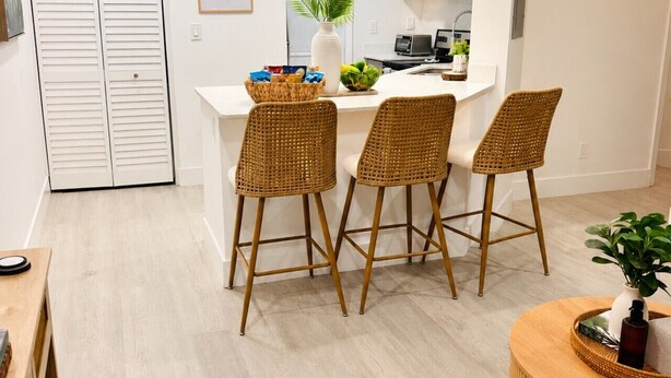 A modern kitchen with white cabinets, a central island, and wicker bar stools. - Casa Tropica Escape | 2BR Near Beach & Airport (Dania Beach)