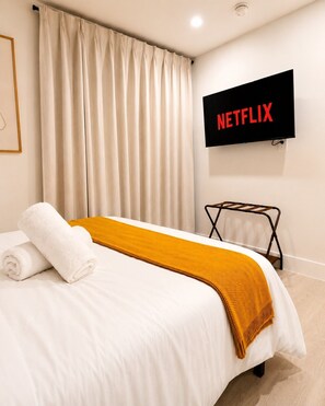 Ein Hotelzimmer mit einem Bett, einem an der Wand montierten Fernseher und einem Fenster mit Vorhängen.