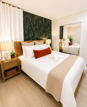 Une chambre d’hôtel avec un grand lit, une table de chevet avec une lampe, un miroir et un mur décoré d’un motif de feuilles vertes.