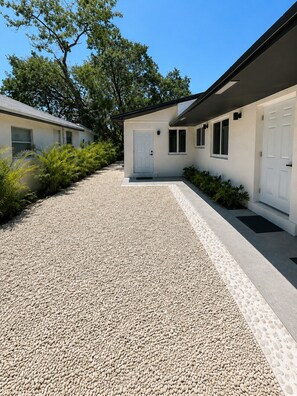 Un bâtiment moderne avec une allée en gravier, des portes blanches et un petit jardin.