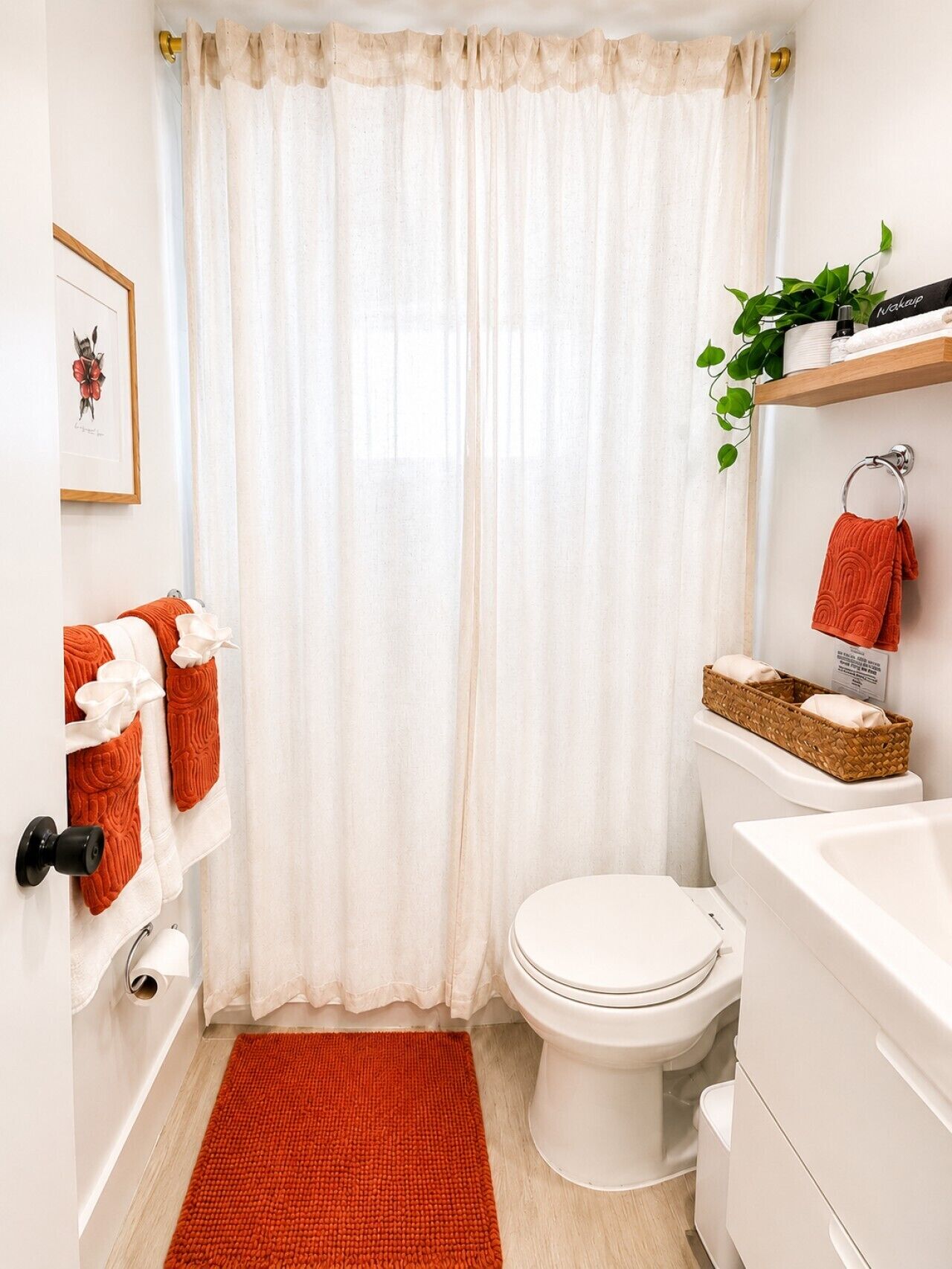 A bathroom with a toilet, a white sink, a red rug, and a shower curtain.