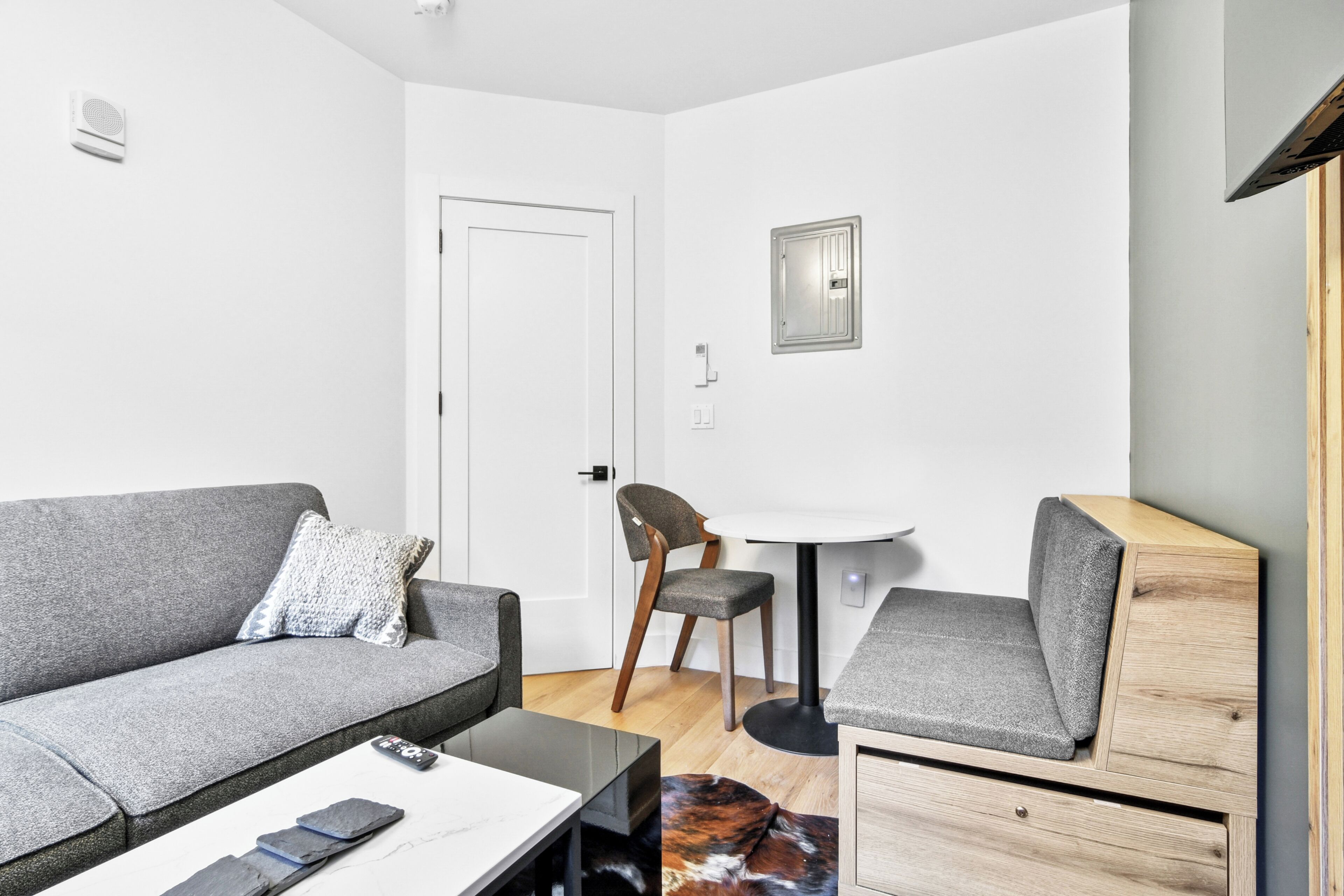 A modern living room with a grey sofa, a small round table, a wooden cabinet, and a chair.