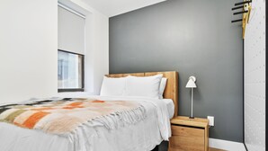 Un dormitorio moderno con una cama grande, una mesita de noche, una lámpara de pared e iluminación integrada.