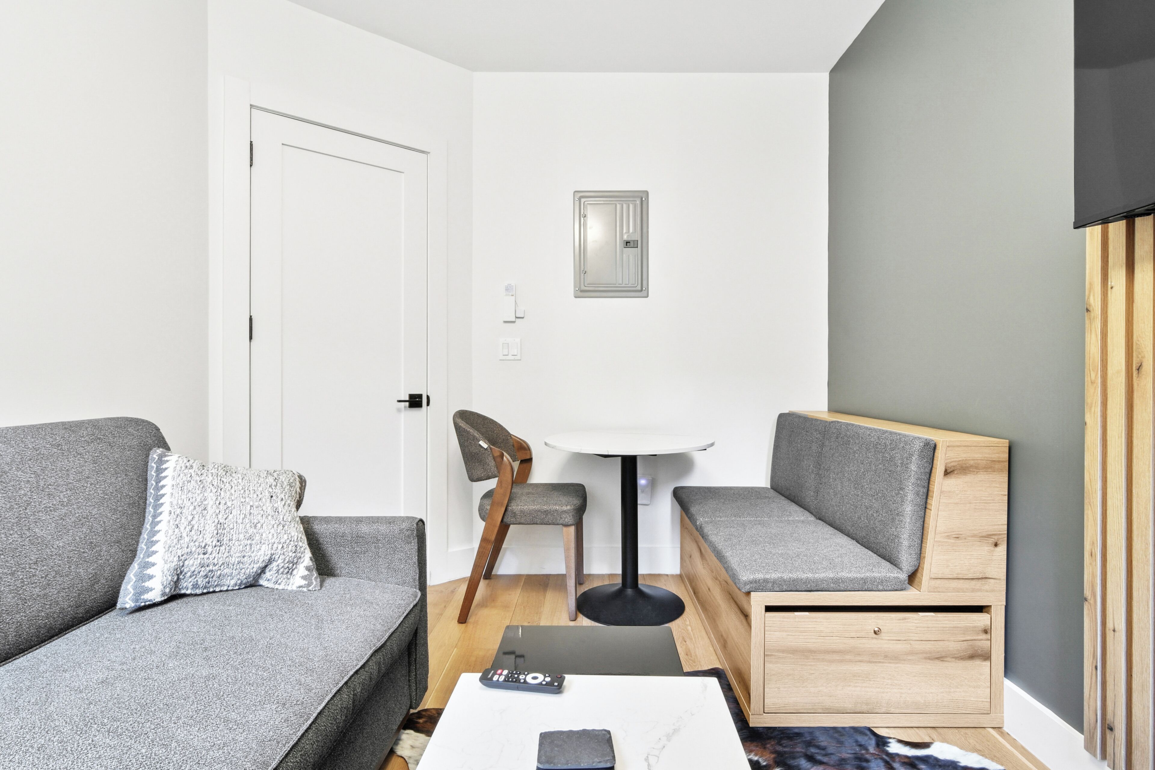 A modern living room with a grey sofa, a small table, a wooden bench, and a chair.