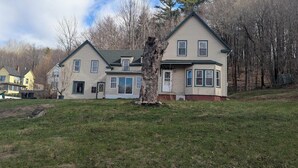 A two-story house with a front porch, a garage, and a large tree in front.