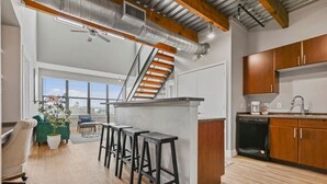 A modern kitchen with wooden cabinets, a dishwasher, and a bar area with stools. - Urban 3-bedroom loft - walk Downtown! (Fort Worth)