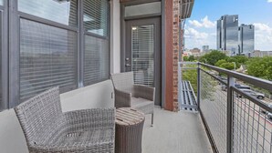 A balcony with wicker furniture, a door, and a view of tall buildings. - Dive into downtown, steps away! (Fort Worth)