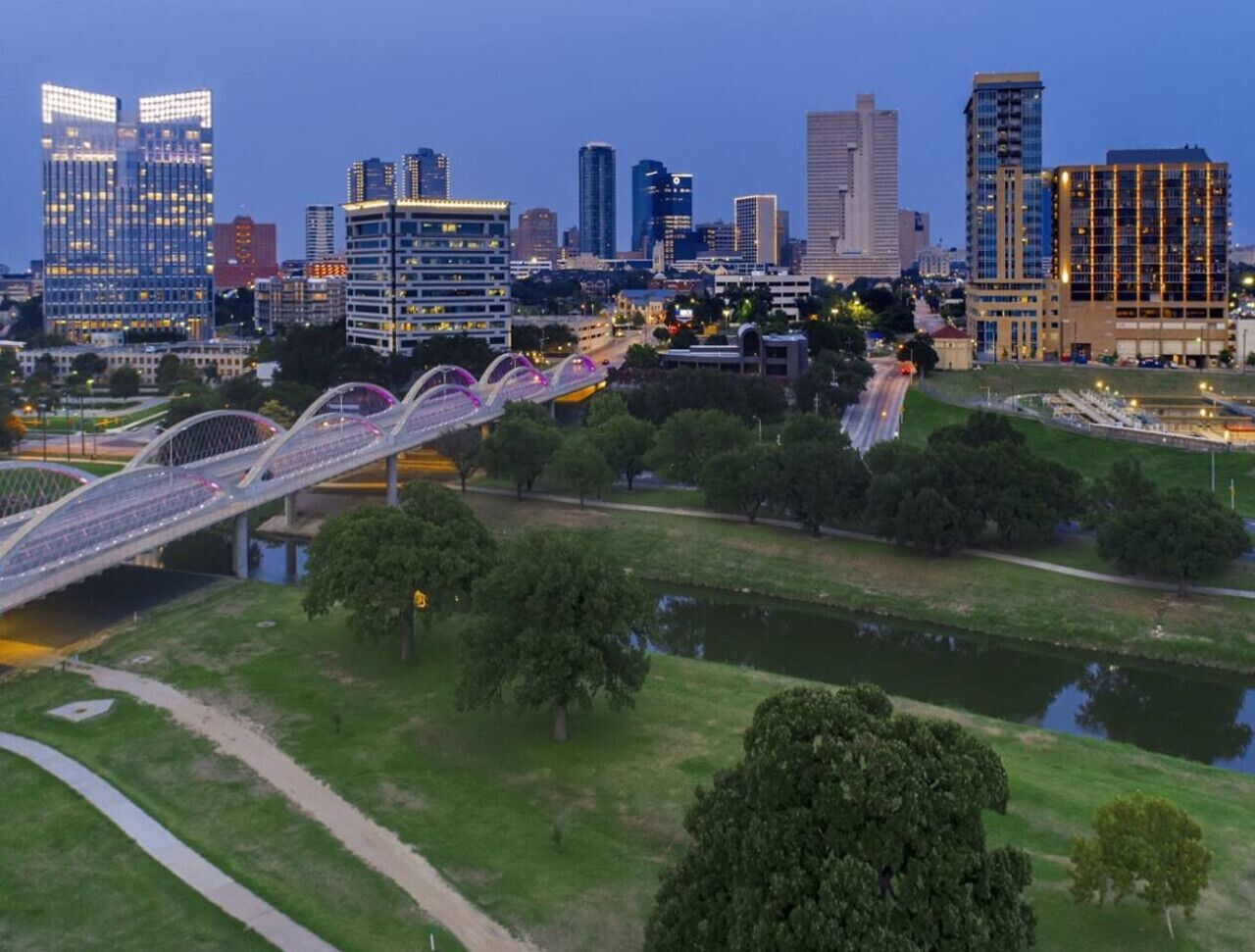 Une vue urbaine avec des bâtiments modernes, un pont piétonnier et un espace vert aménagé en parc.