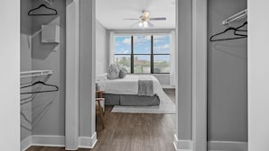 A bedroom with a bed, a window with blinds, a ceiling fan, and a closet with hanging clothes.