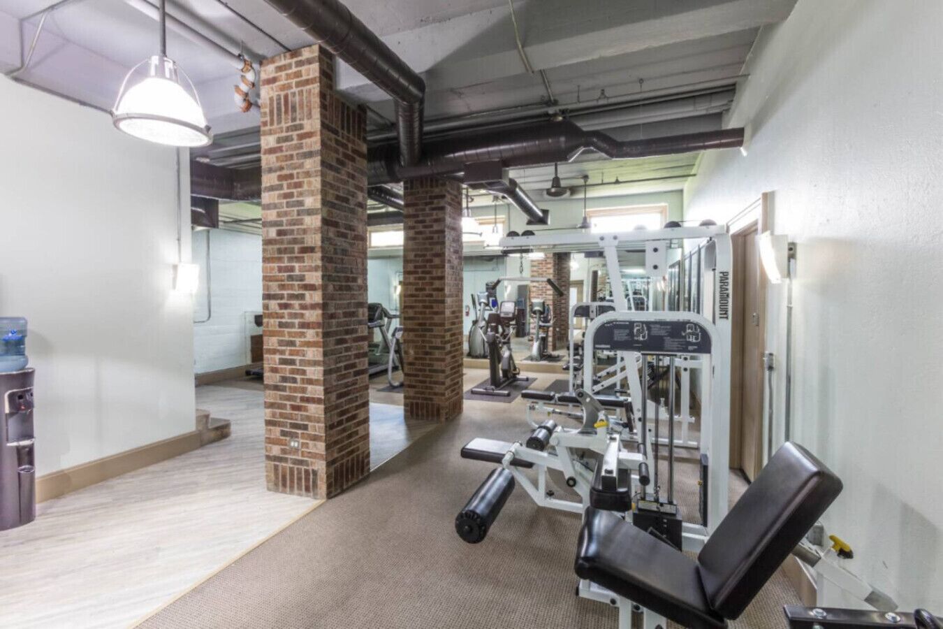 A gym with brick pillars, exercise machines, and a water dispenser.