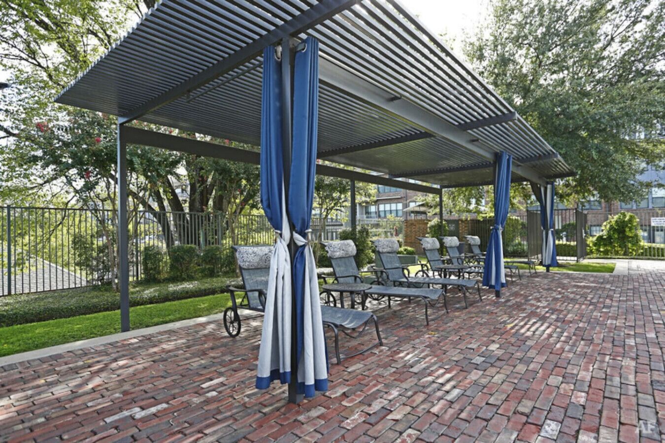 A covered outdoor seating area with brick flooring and metal railings.