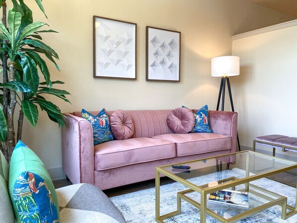 Un salon avec un canapé rose, une table basse en verre, un lampadaire et deux tableaux encadrés accrochés au mur.