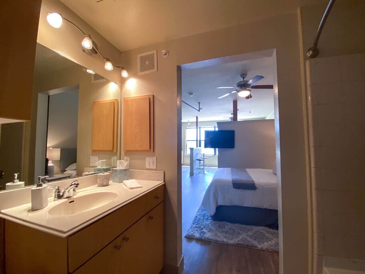 A hotel room with a bathroom, a bed, a ceiling fan, and a TV.