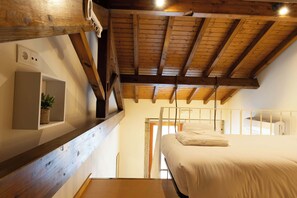 A bedroom with a wooden ceiling, a bed, a bedside table, and a small shelf with a plant.