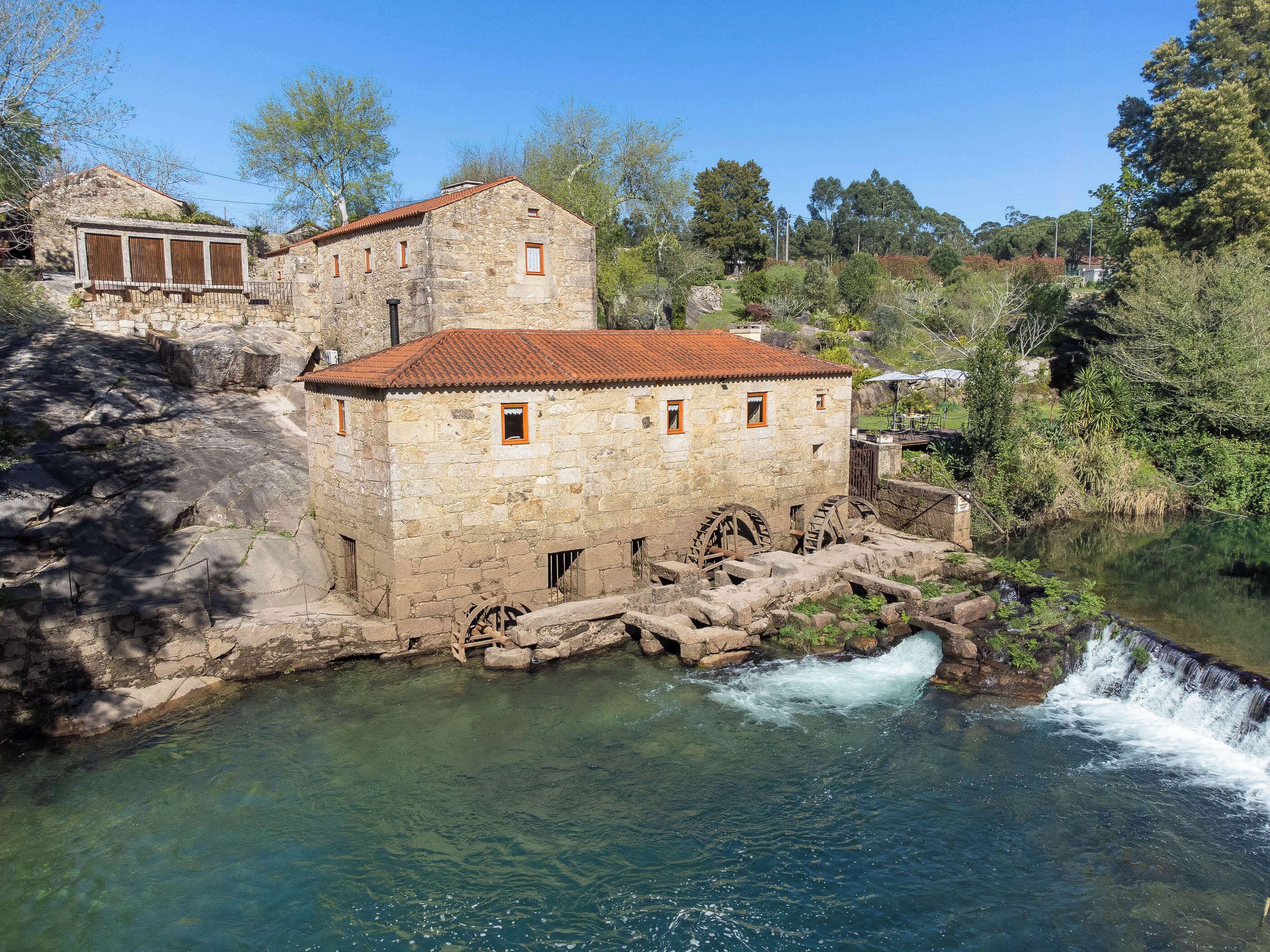 Un bâtiment en pierre avec un toit recouvert de tuiles rouges, de grandes roues à eau et un ruisseau aux eaux claires.