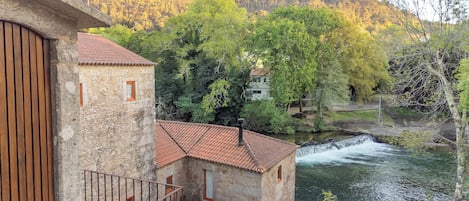 A stone building with a red-tiled roof, a wooden fence, and a river in the background.