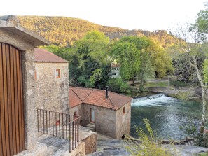 Ein Steinhaus mit rotem Ziegeldach, einem Holzzaun und einem Fluss im Hintergrund.