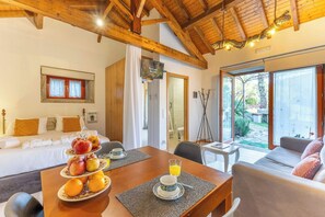 Ein Zimmer mit Holzboden, einem Bett, einem Esstisch mit Obst und einer Tasse sowie einem Sofa.