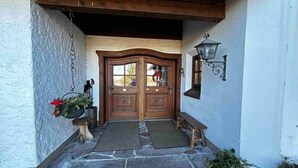 A wooden double door with glass panels, a stone floor, a wooden bench, a wall-mounted lantern, and a hanging chain. - Lake and Mountain view (Seeg)