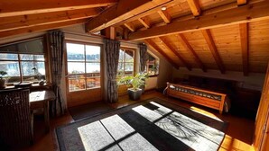 A room with a sloped ceiling, large windows, a wooden bench, and a potted plant. - Lake and Mountain view (Seeg)