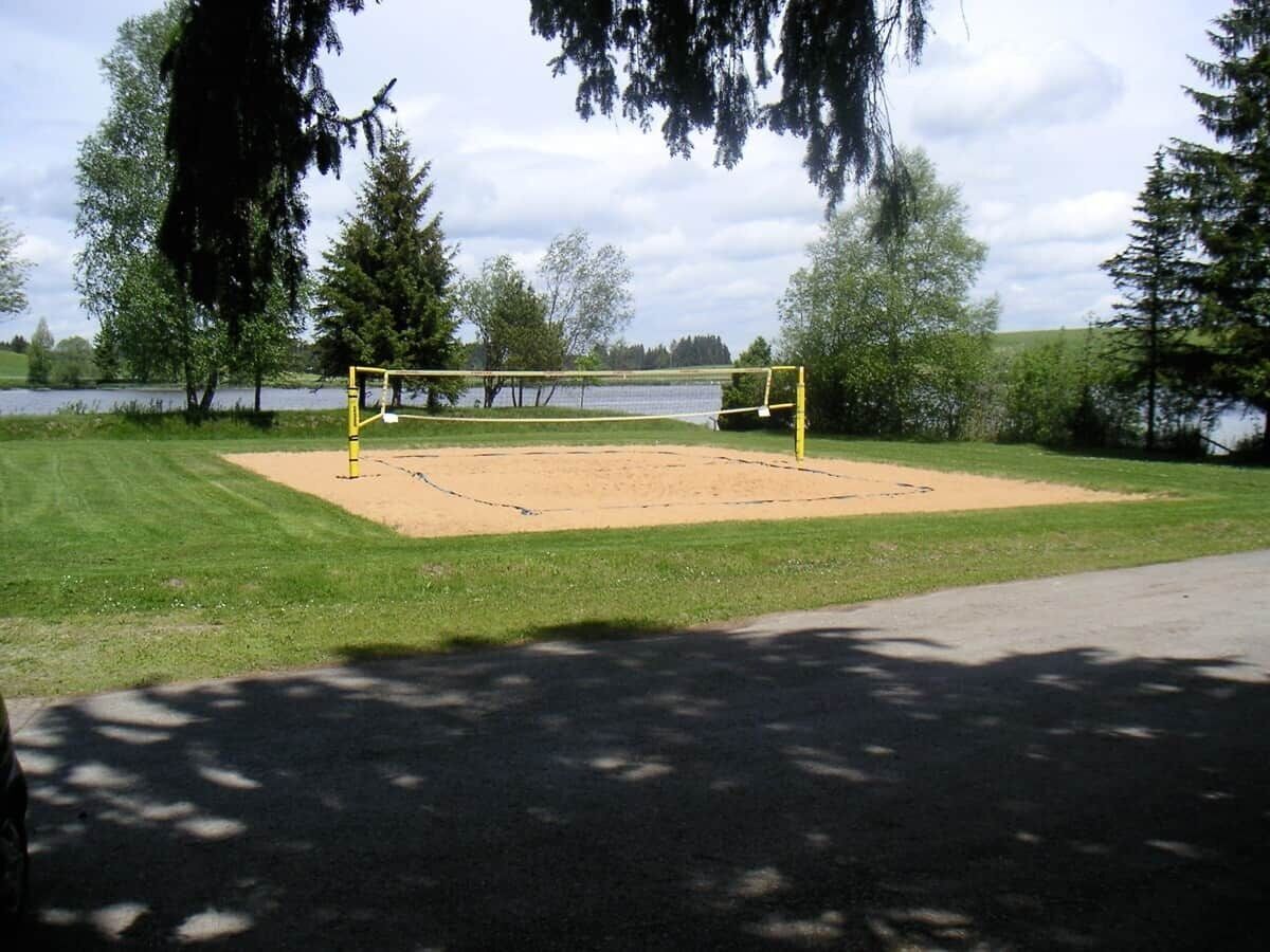 En volleybollplan med ett nät, omgiven av träd och en vattenyta.