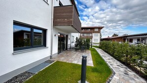 A modern residential building with a paved patio, a small garden, and a clear sky. - Holiday apartment Wiesenweg (Seeg)