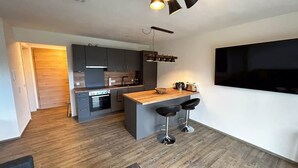 A modern kitchen with dark cabinets, a wooden island, and a built-in TV. - Holiday apartment Wiesenweg (Seeg)