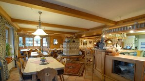 A traditional kitchen with wooden beams, a dining area with a chandelier, and a bar area with a large window. - Holiday apartment Wiesenweg (Seeg)