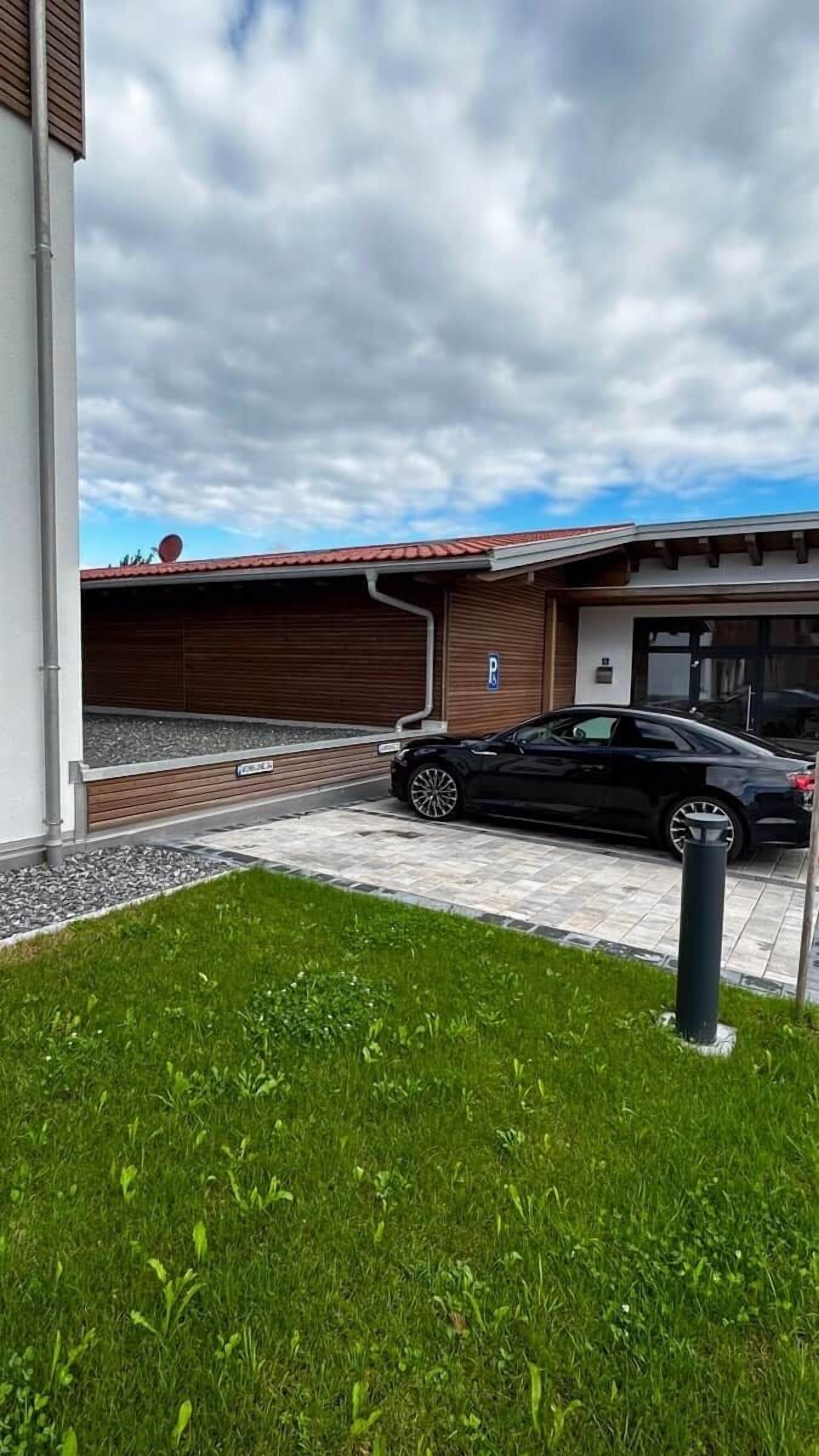 A parking area with a black car, a building with a red roof, and a grassy foreground.
