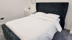 Un letto rifatto con cura, una testata scura, un comodino con un vaso e una parete bianca e semplice.