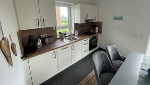 Una cucina moderna con mobili bianchi, un piano di lavoro in legno, un lavello, un fornello e un'area pranzo con tavolo e sedie.