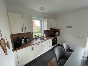 Une cuisine moderne avec des meubles blancs, un plan de travail en bois, un évier, une cuisinière et un coin repas comprenant une table et des chaises.