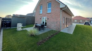 Una casa a due piani in mattoni con un patio, un garage e un prato ben curato.