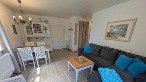 Ein Wohnzimmer mit einem dunklen Sofa, einem Holztisch und einem weißen Esstisch mit Stühlen.
