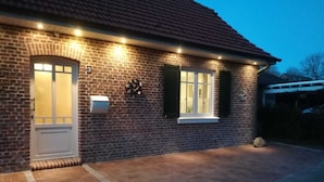 Ein Backsteinhaus mit weißer Tür, einem Briefkasten und einem kleinen Fenster mit Fensterläden.