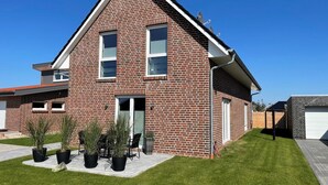 A two-story house with a brick exterior, a front door, and a small front yard with potted plants. - Modern vacation home just 100 m from the Wangermeer with two bedrooms, smart TVs, fiber optics and terrace - perfect for families and those seeking relaxation. (Wangerland)