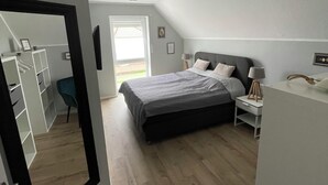 A bedroom with a bed, bedside table, lamp, and a view of the outside. - Modern vacation home just 100 m from the Wangermeer with two bedrooms, smart TVs, fiber optics and terrace - perfect for families and those seeking relaxation. (Wangerland)