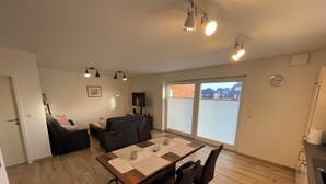 Ett vardagsrum med en soffa, en tv, ett matbord med stolar och en skjutdörr i glas som leder ut till uteplatsen.