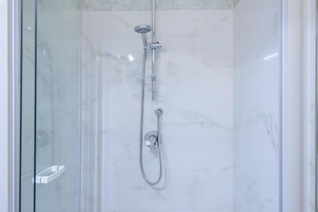 A glass-enclosed shower with a handheld showerhead and a fixed wall-mounted faucet.