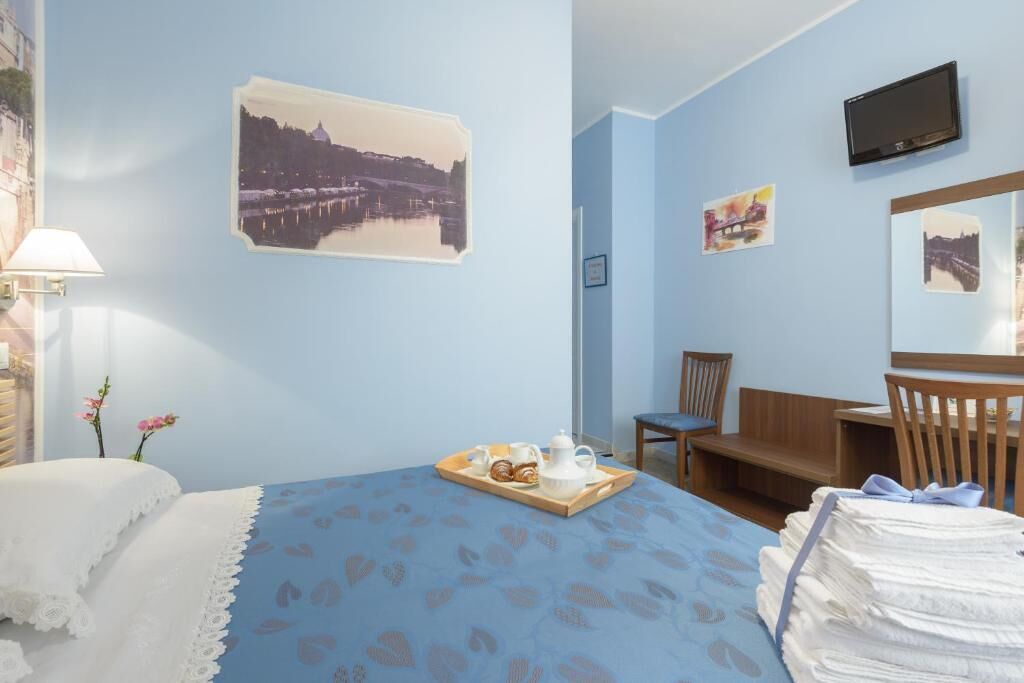 Habitación de hotel con cama, escritorio, silla, televisión y un muro decorado con imágenes.