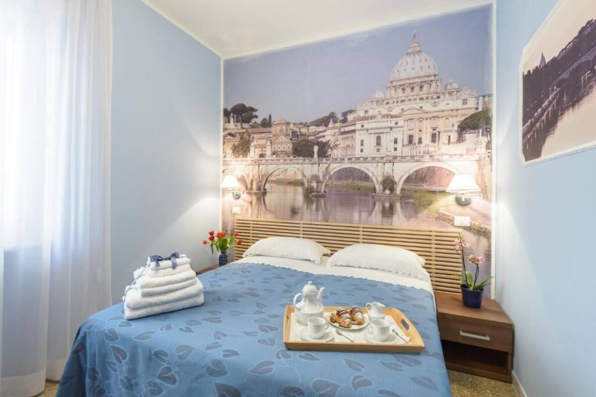A hotel room with a bed, a tray with breakfast items, and a mural of a historic building.